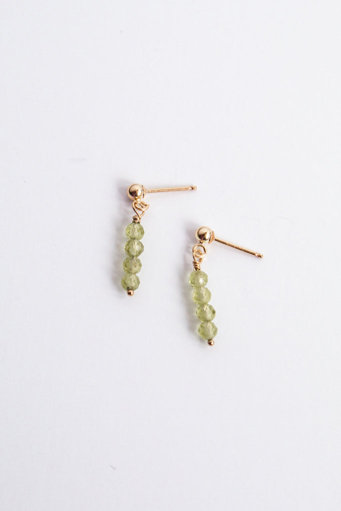 Moment and Milestone stud earrings in 14k gold filled and dangling peridot gemstones, symbolizing life’s meaningful moments, displayed on a white background.