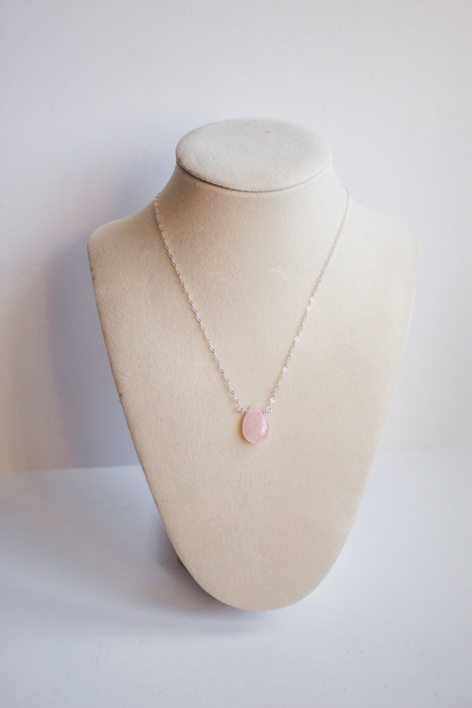 AAA-quality rose quartz teardrop necklace, highlighting the soft pink stone on a cream jewelry stand.