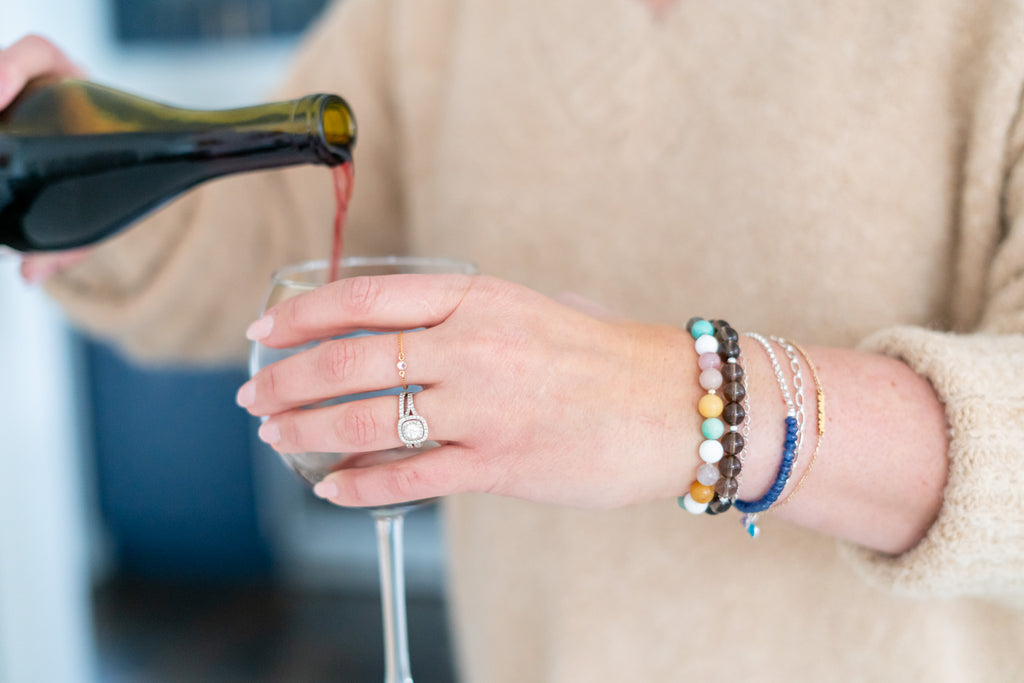 Model pouring a glass of wine wearing a beautiful gemstone and chain bracelet stack. 