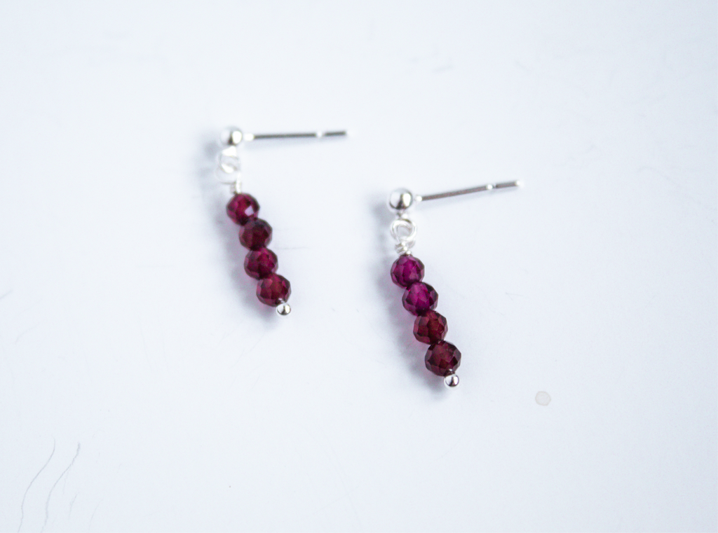 Moment and Milestone stud earrings in sterling silver and dangling garnet gemstones, symbolizing life’s meaningful moments, displayed on a white background.