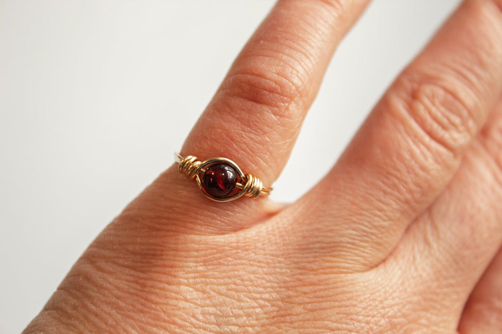 Model wearing a 14k gold filled wire-wrapped ring featuring a garnet gemstone on a pinky.