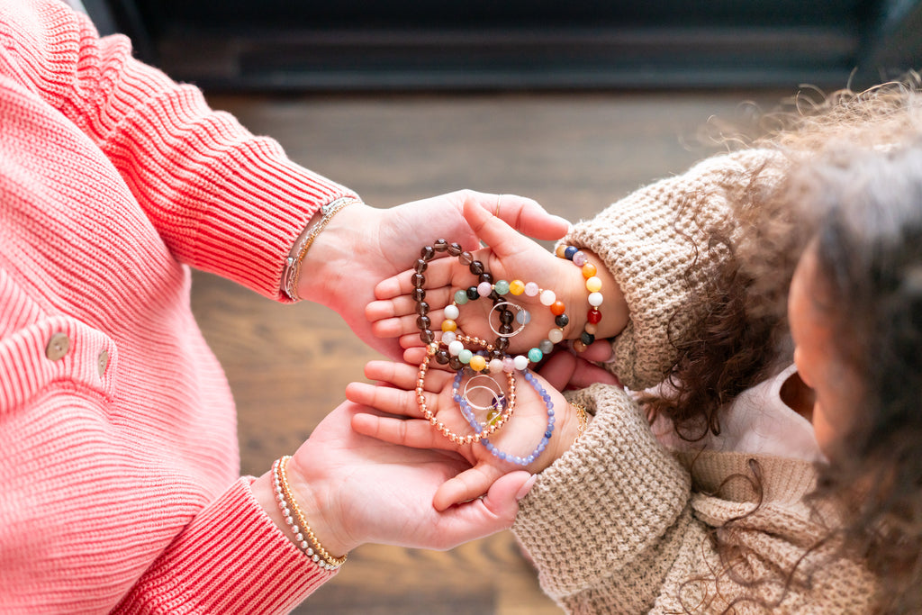 Olivia and Becky, the owner, holding some of their handmade pieces with their hands stacked on top of each other.