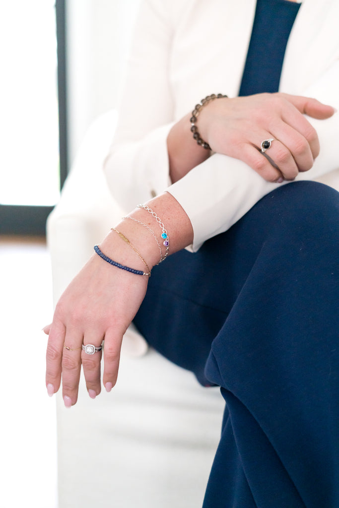 Model in white jacket and nave slacks is wearing several jewelry pieces from The Always Busy Mama. This includes a ring and bracelets.