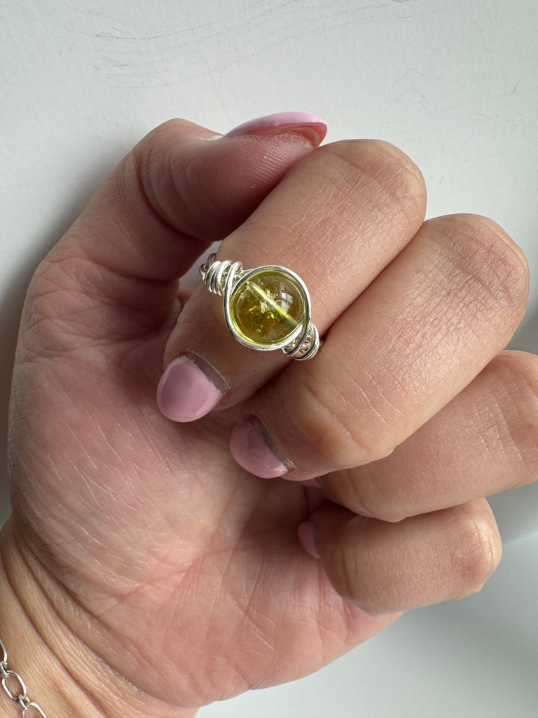 A Sterling Silver wire-wrapped ring featuring a peridot gemstone displayed on a model’s finger.