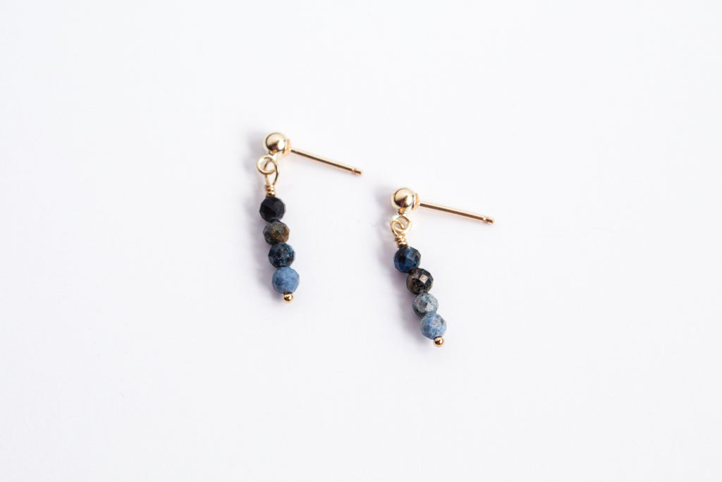 Moment and Milestone stud earrings in 14k gold filled and dangling sapphire gemstones, symbolizing life’s meaningful moments, displayed on a white background.