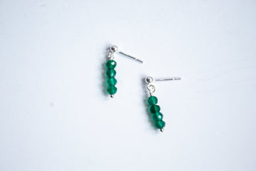 Moment and Milestone stud earrings in sterling silver and dangling emerald gemstones, symbolizing life’s meaningful moments, displayed on a white background